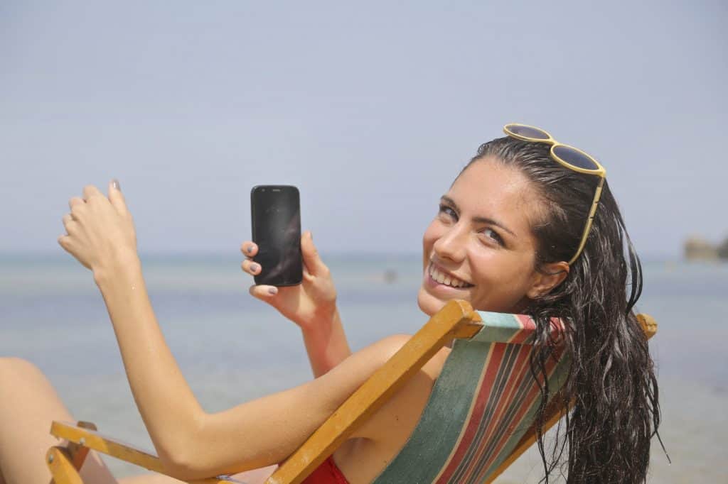 This happy girl is enjoying herself at the beach as she holds her phone.