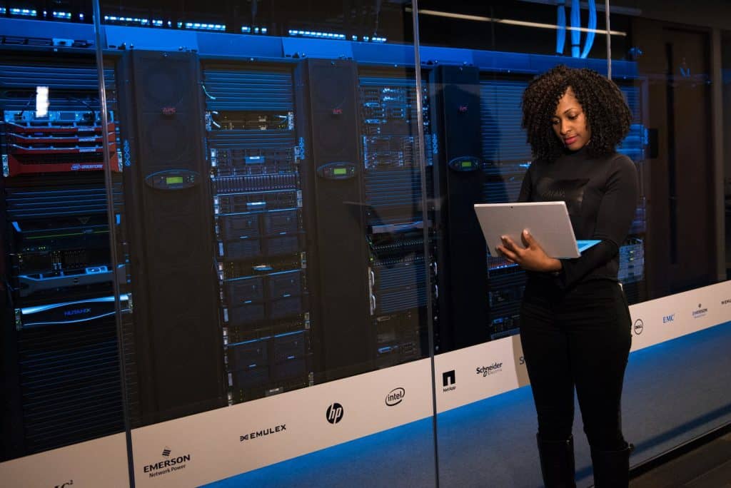 A woman holding a laptop in front of many computers