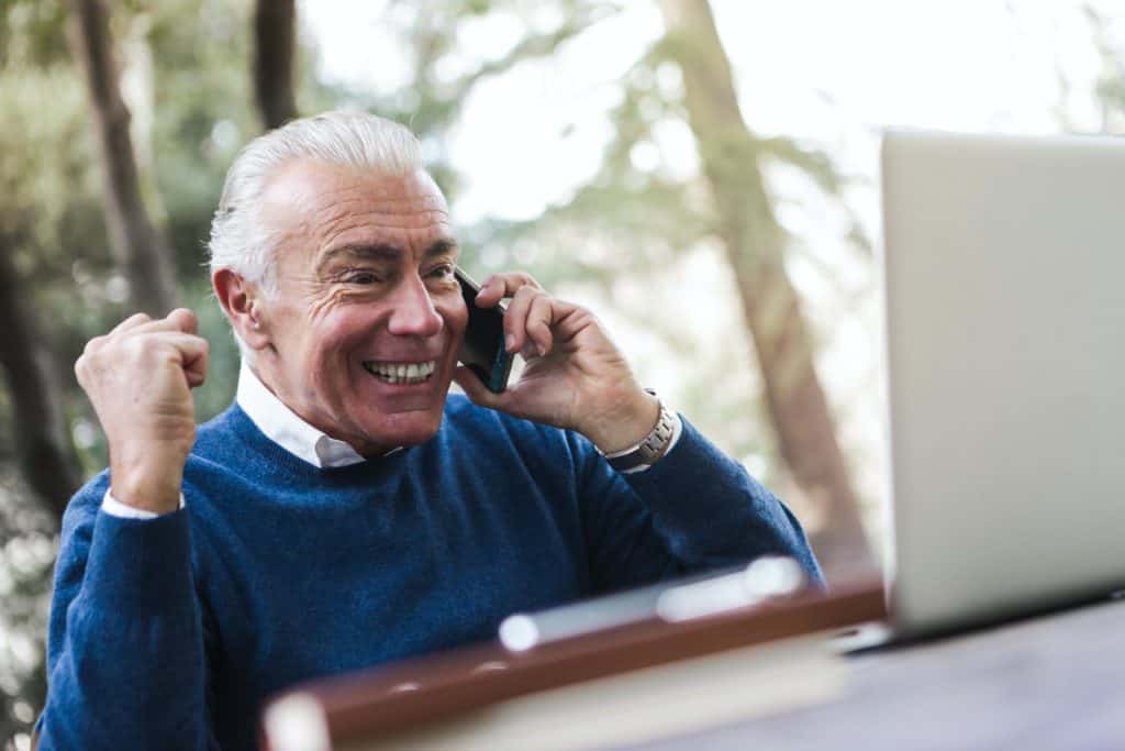 An elderly man smiling as he makes a phone call