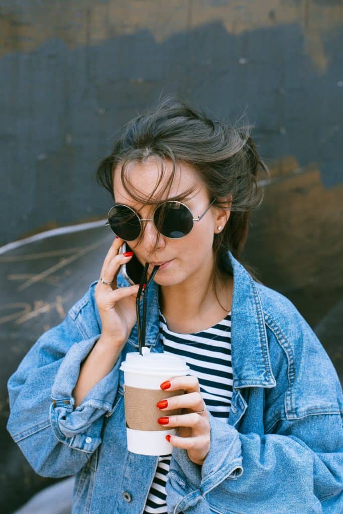 A trendy woman with sunglasses and a jean jacket holding a disposable cup