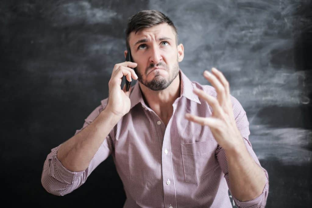 A stressed out and frustrated man in a pink dress shirt on the phone