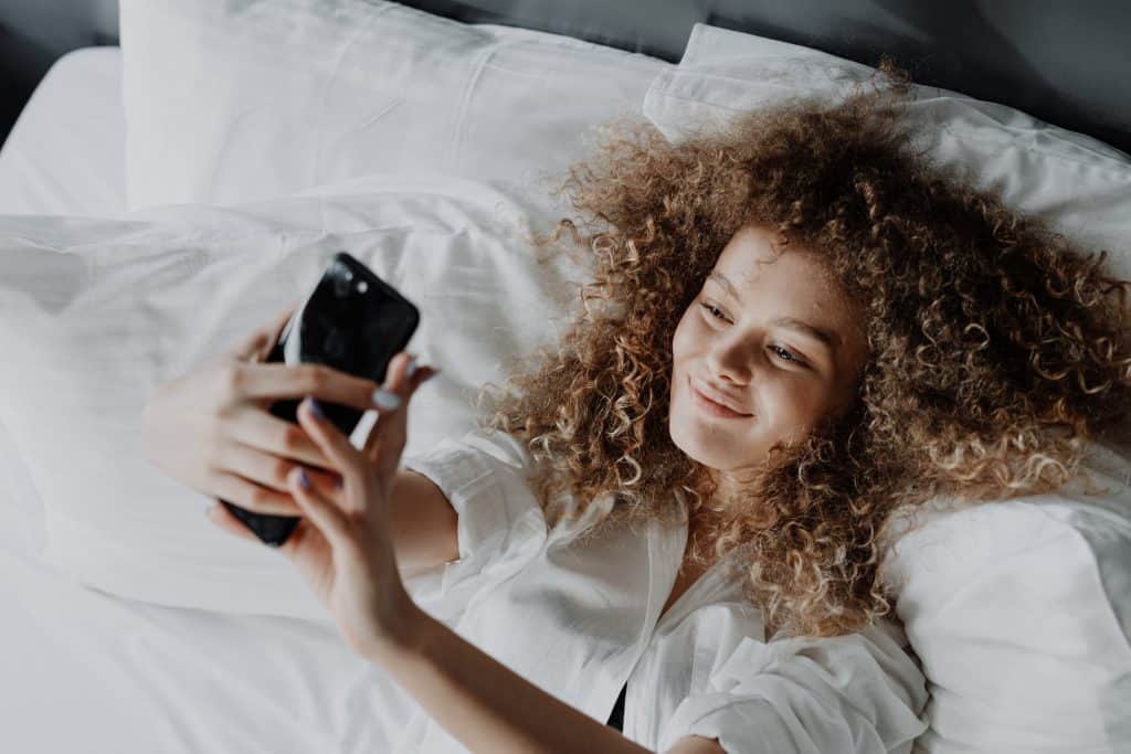 A curly haired woman taking a selfie in bed