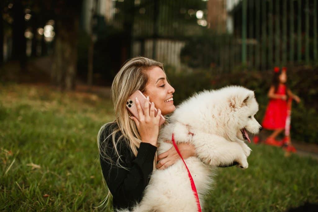 A woman holding a white dog as she talks on the phone 