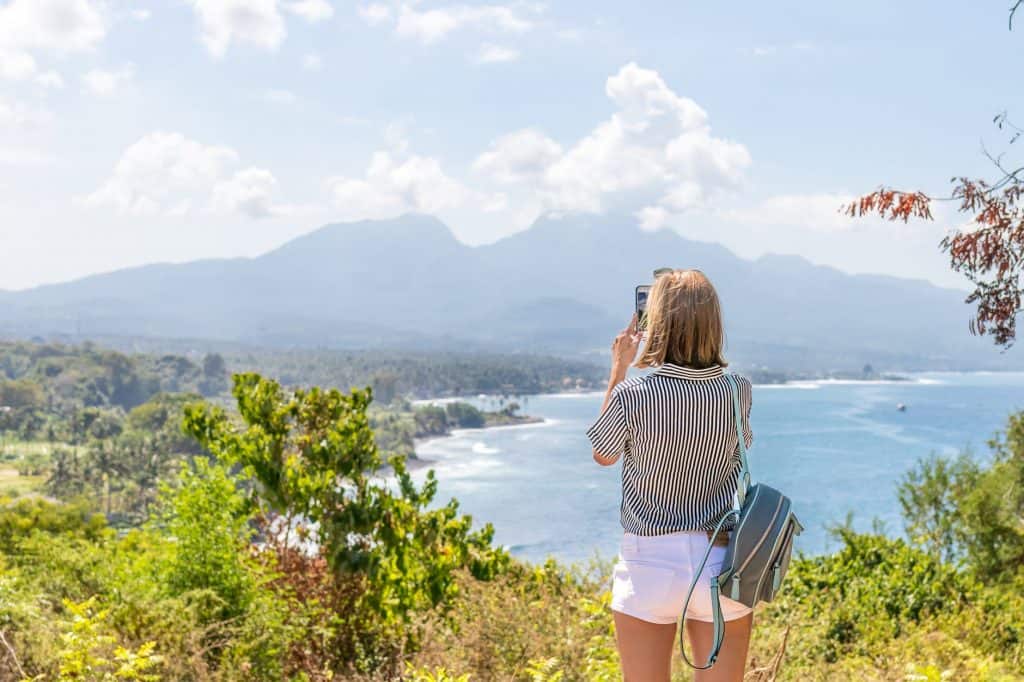 A girl standing over a lake and taking a picture 