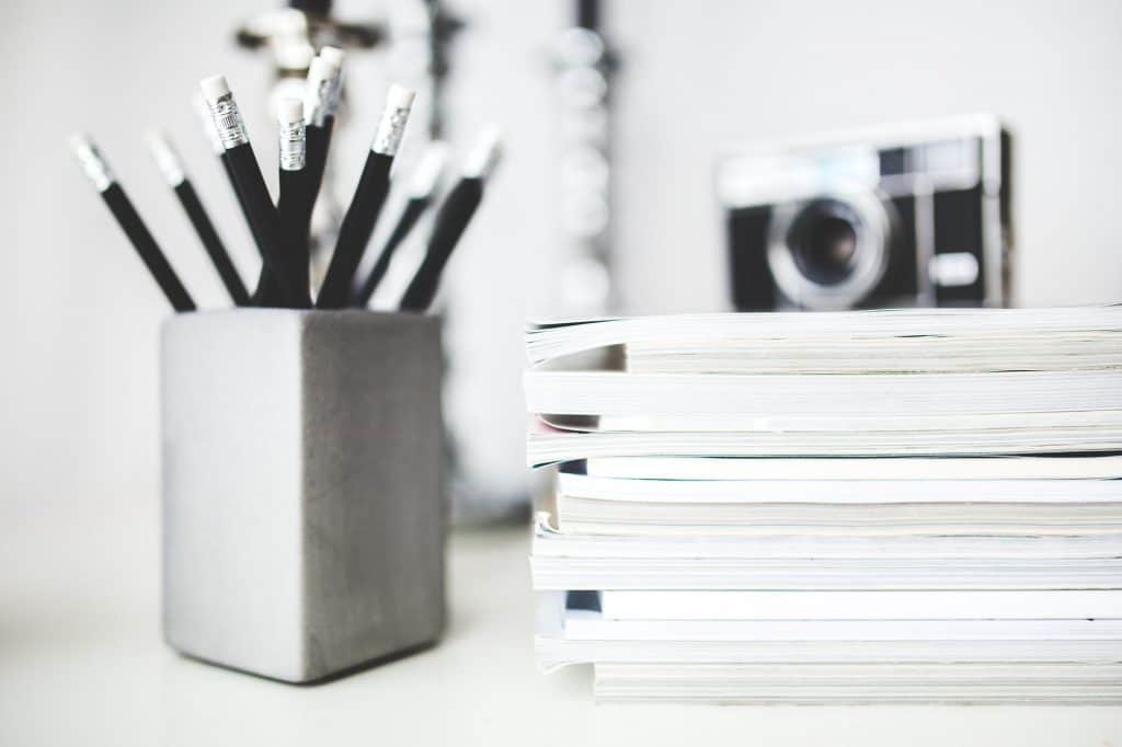 A pile of magazines next to a jar of pencils