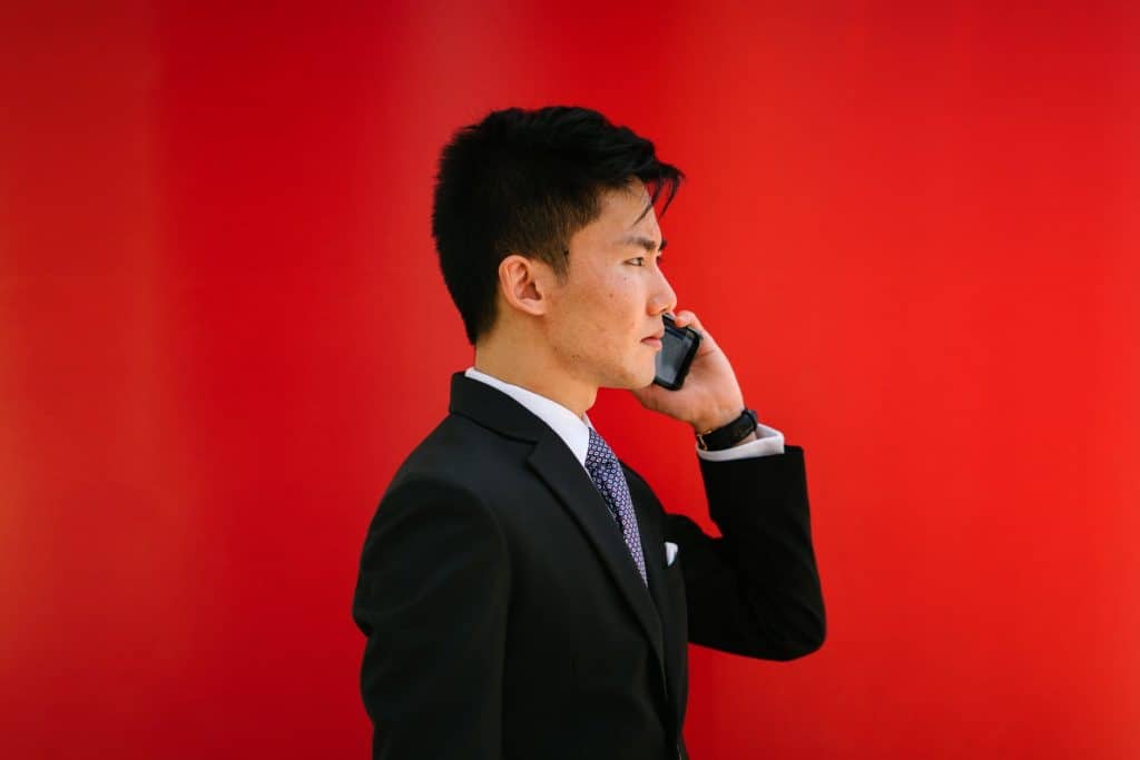 An Asian man in a suit talking on the phone in front of a red background