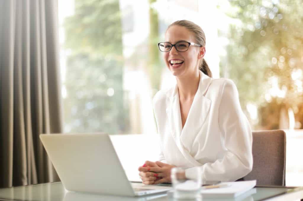 A woman wearing white smiling and laughing at her desk 