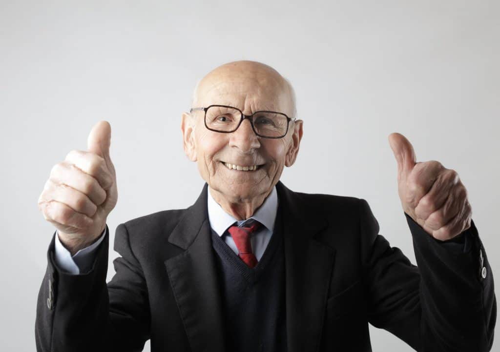 An elderly man dressed in a suit with his thumbs up 