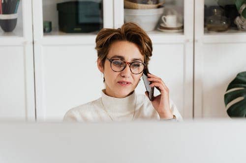 A woman with short hair and glasses speaking on the phone 