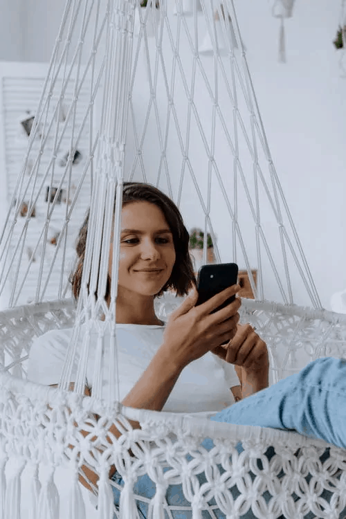 A woman smiling in a hammock with her phone 