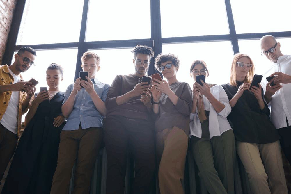 A group of people standing by the window holding their phones