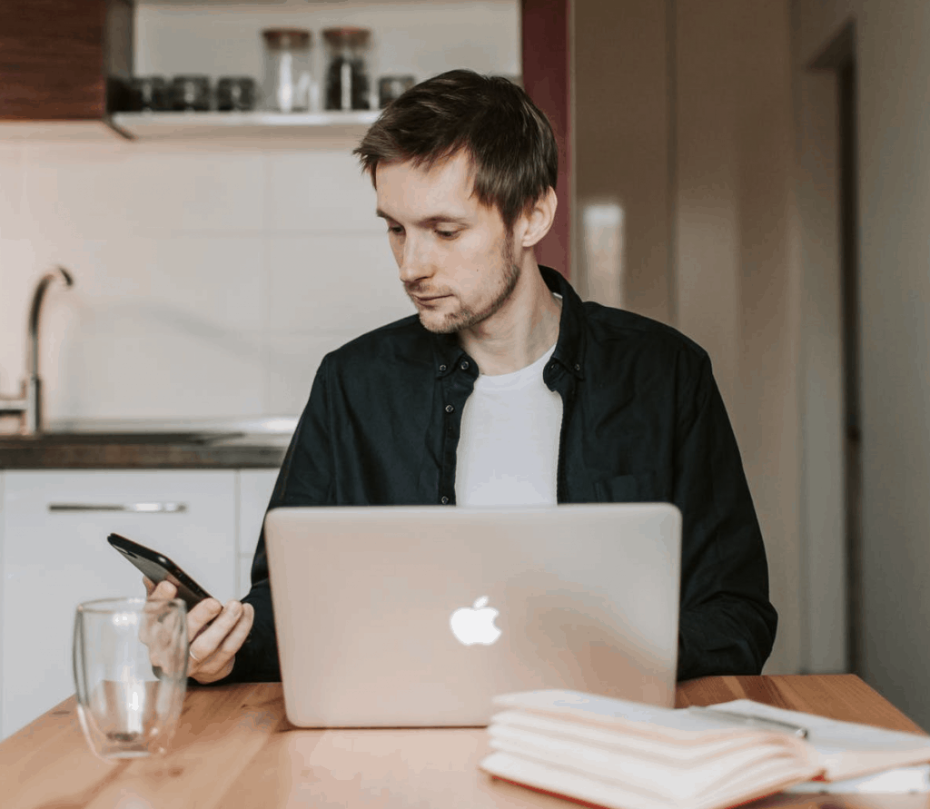 A man checking his phone in front of his laptop 