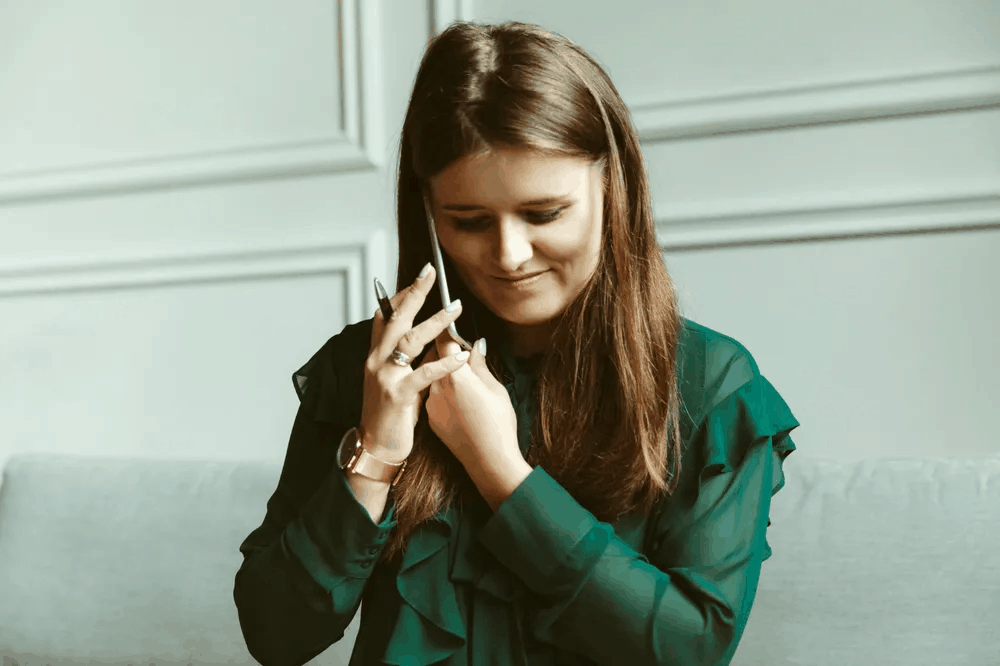 A young woman in an olive green shirt speaking on the phone