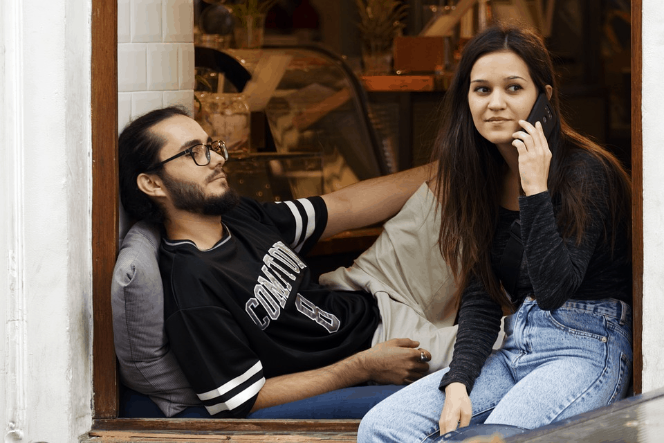 A couple sitting on a ledge speaking on the phone