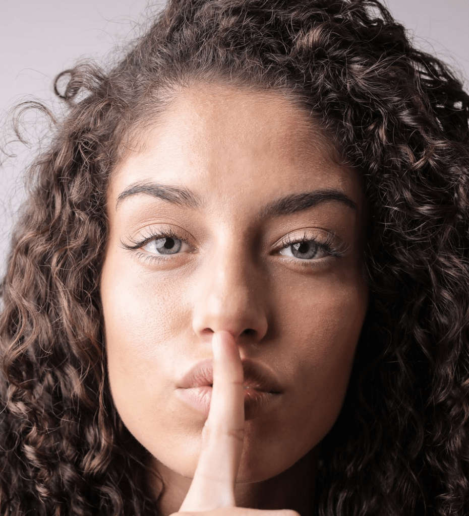 A woman with curly brown hair with her finger on her lips