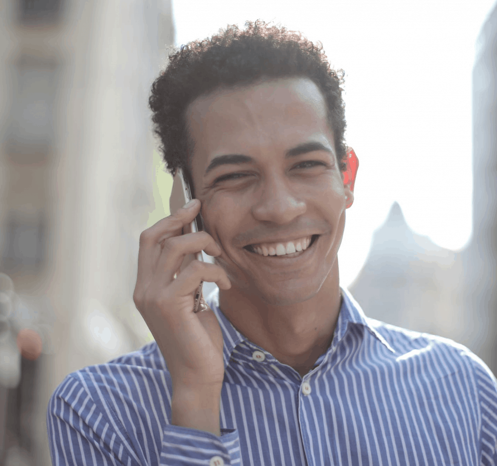 A man in a stripped dress shirt smiling on the phone