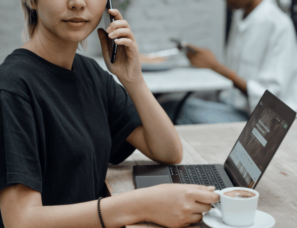 A woman speaking on the phone in front of her laptop with a cup of coffee