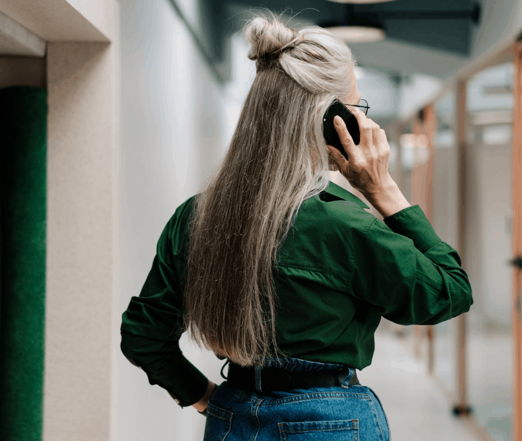 The back of a woman with long gray hair speaking on the phone