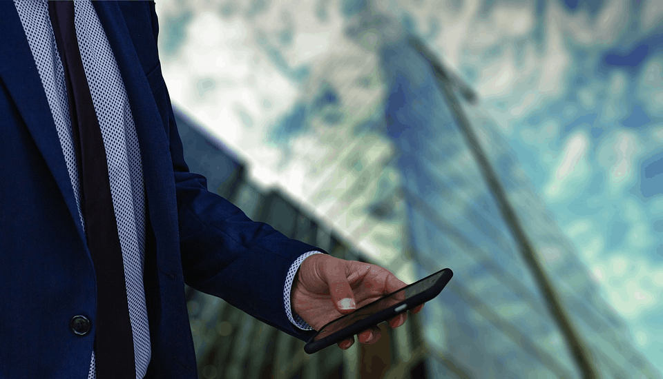 A buisnessman holding a phone in front of a tall building 