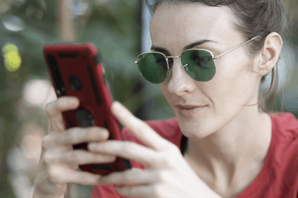 A woman wearing sunglasses holding a smartphone