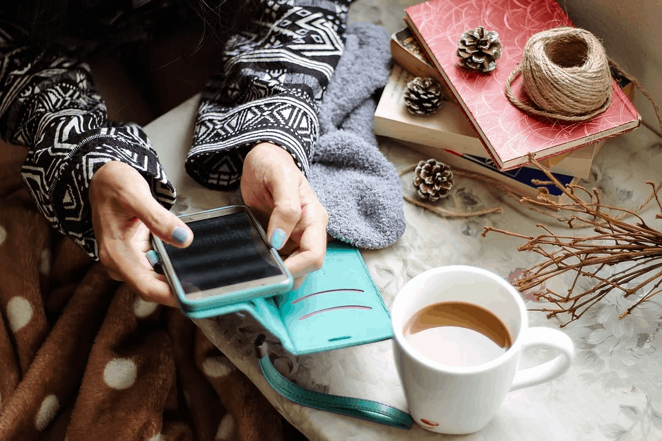 A girl in a wool sweater holding a smartphone at her desk