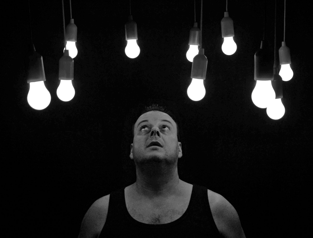 A man in a black tank top looking up at light bulbs 