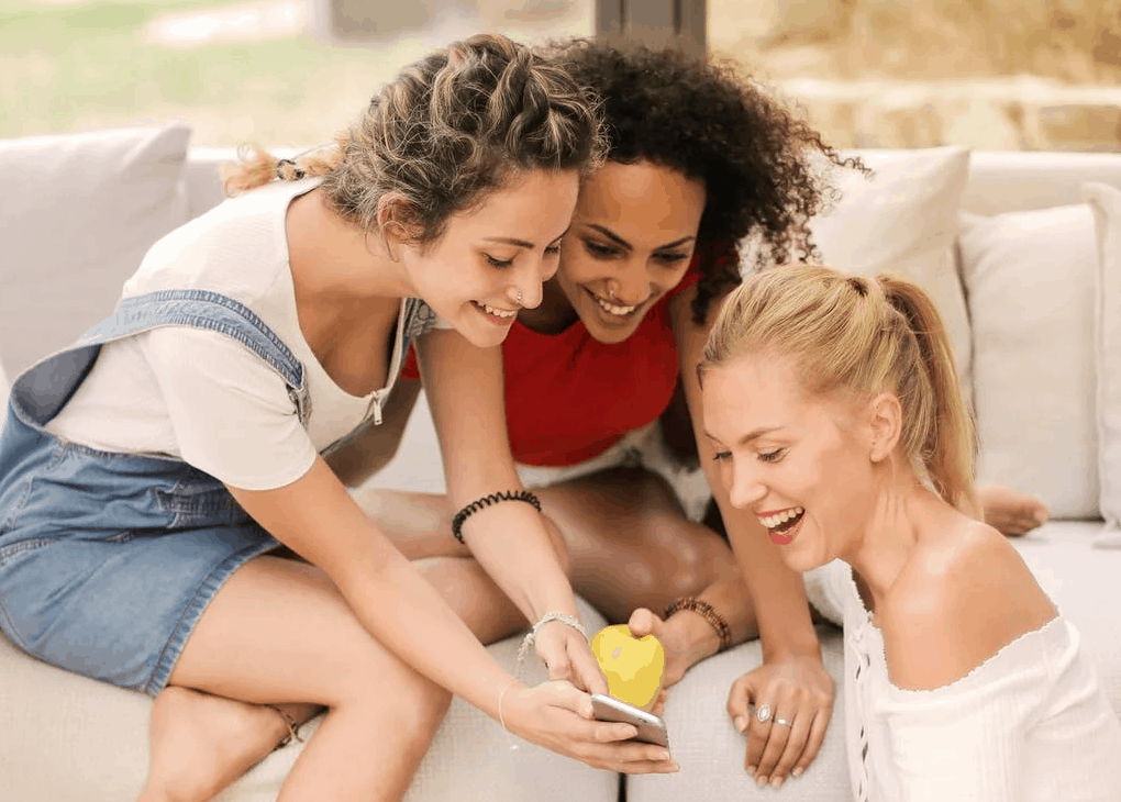 Three girls smiling and laughing as they hold the phone