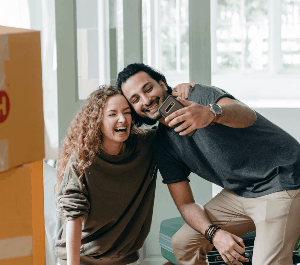 A couple holding a phone together smiling at it 