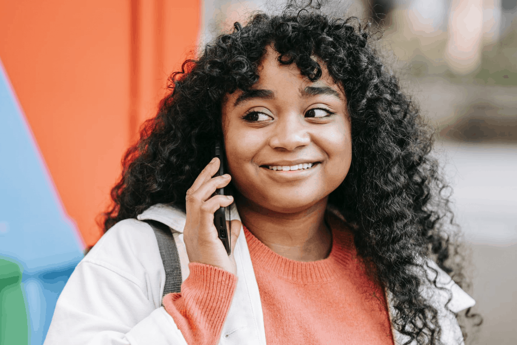 A girl with curly brown hair smiling on the phone