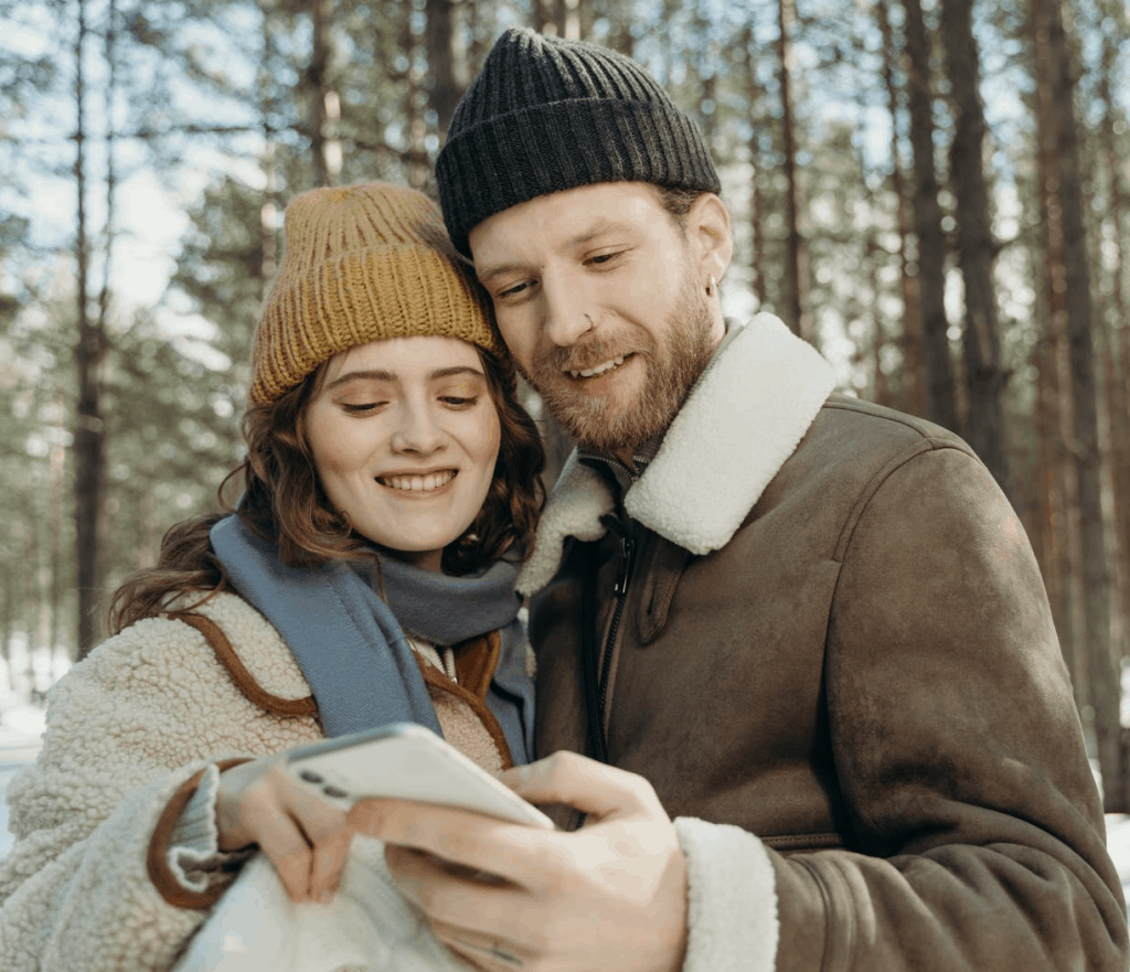 A couple smiling at a phone together in the winter cold