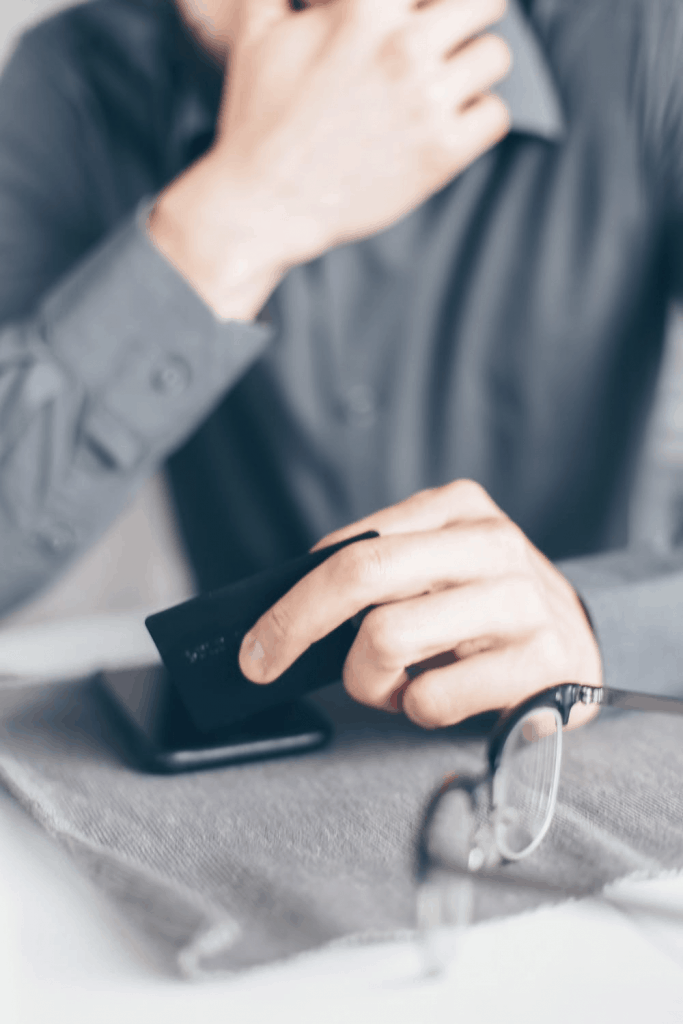 A man holding his credit card and phone as he sits at his desk